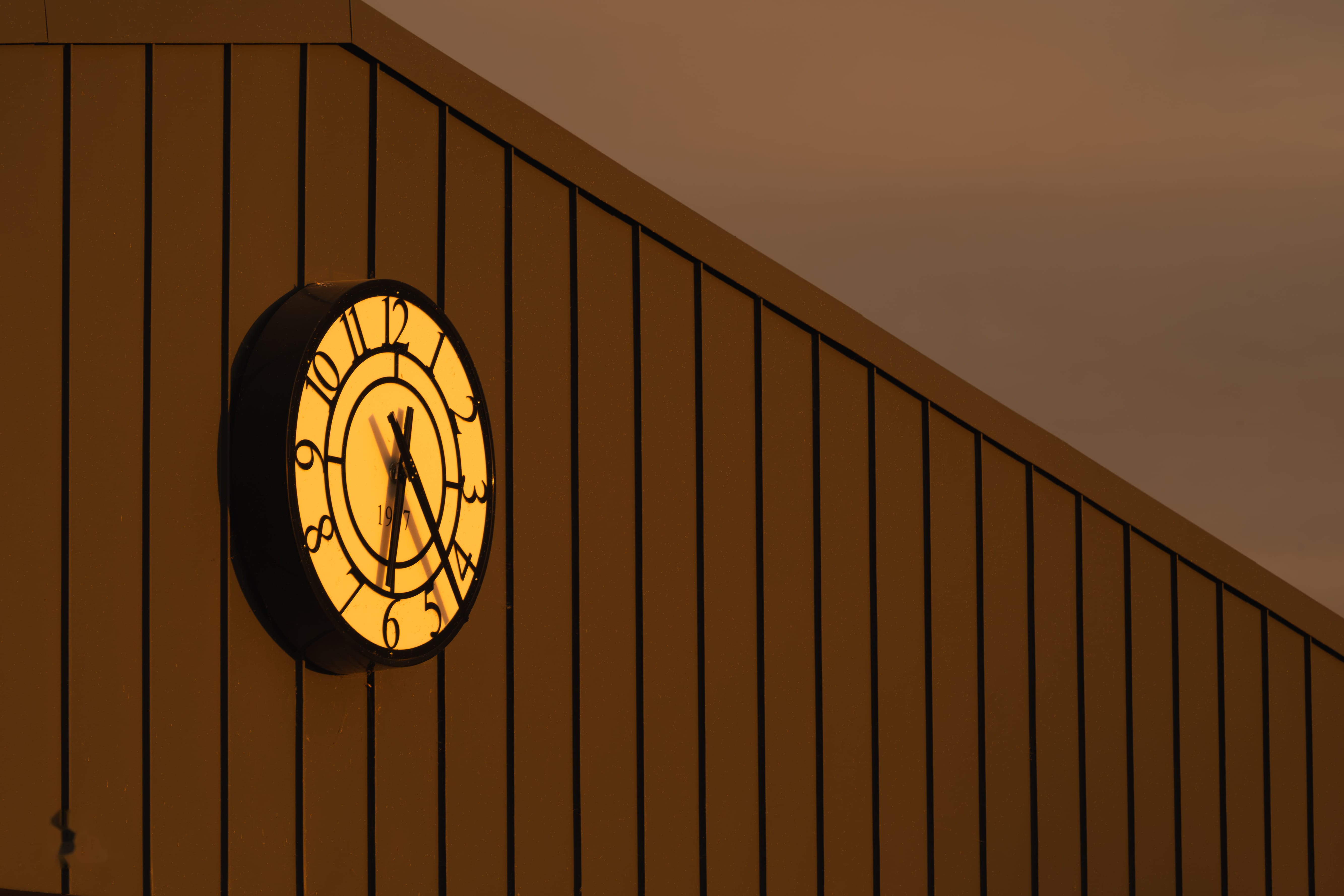 An illuminated clock reading 1907 mounted on the Academy building's cladding at dusk