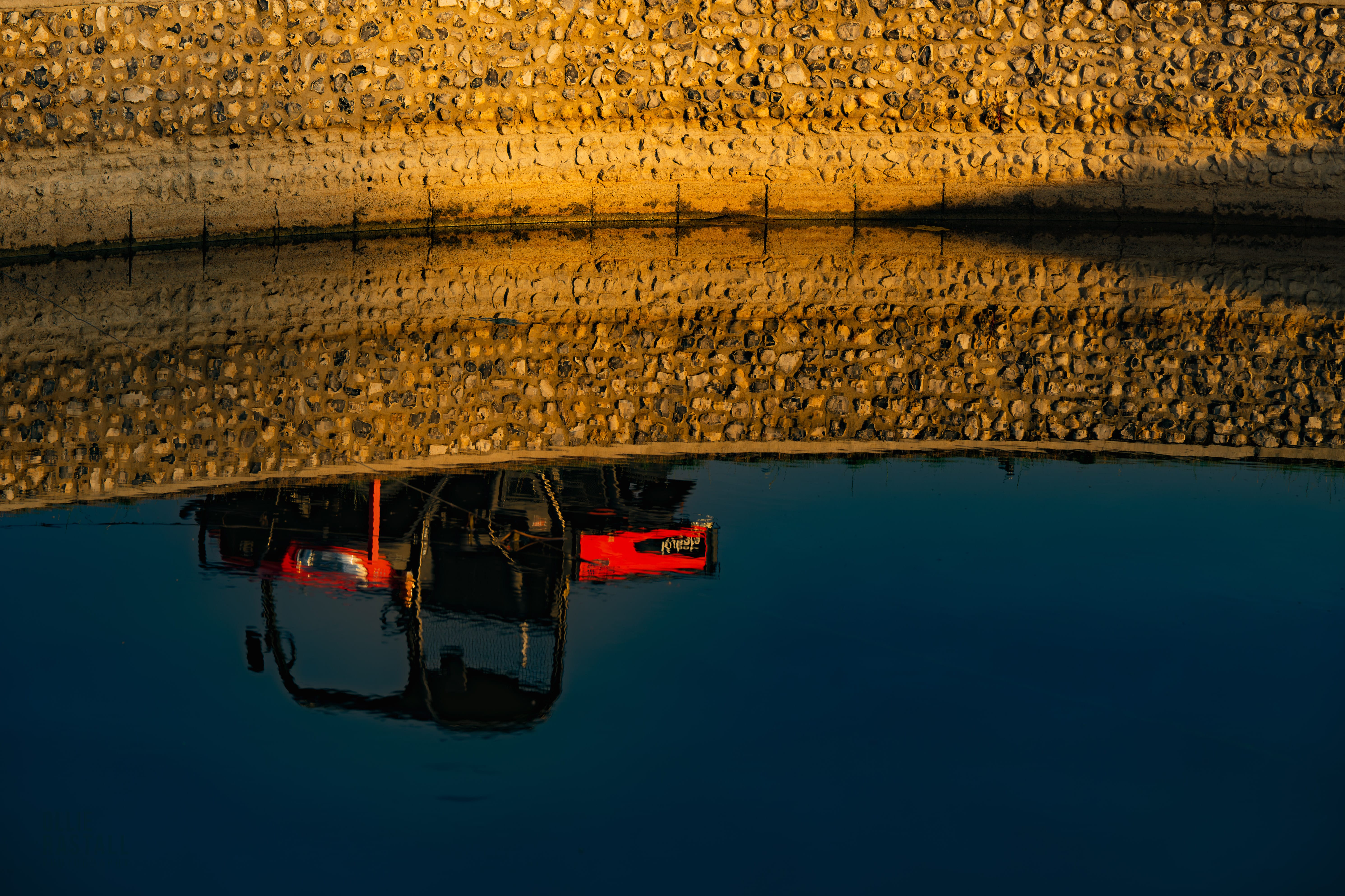 A mower reflected in the still water of a pond