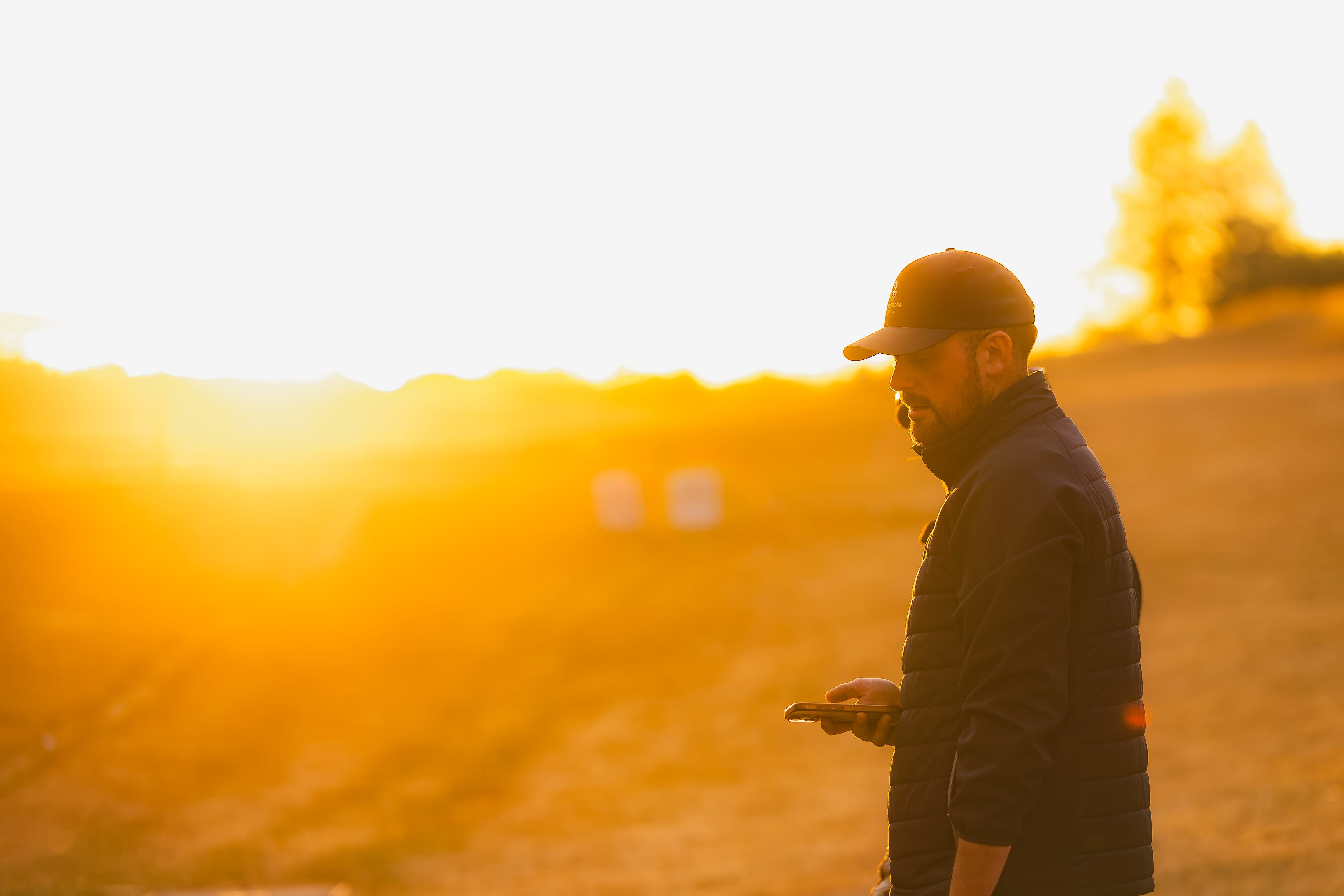 A staff member checking his phone on the driving range at sunset, backlit