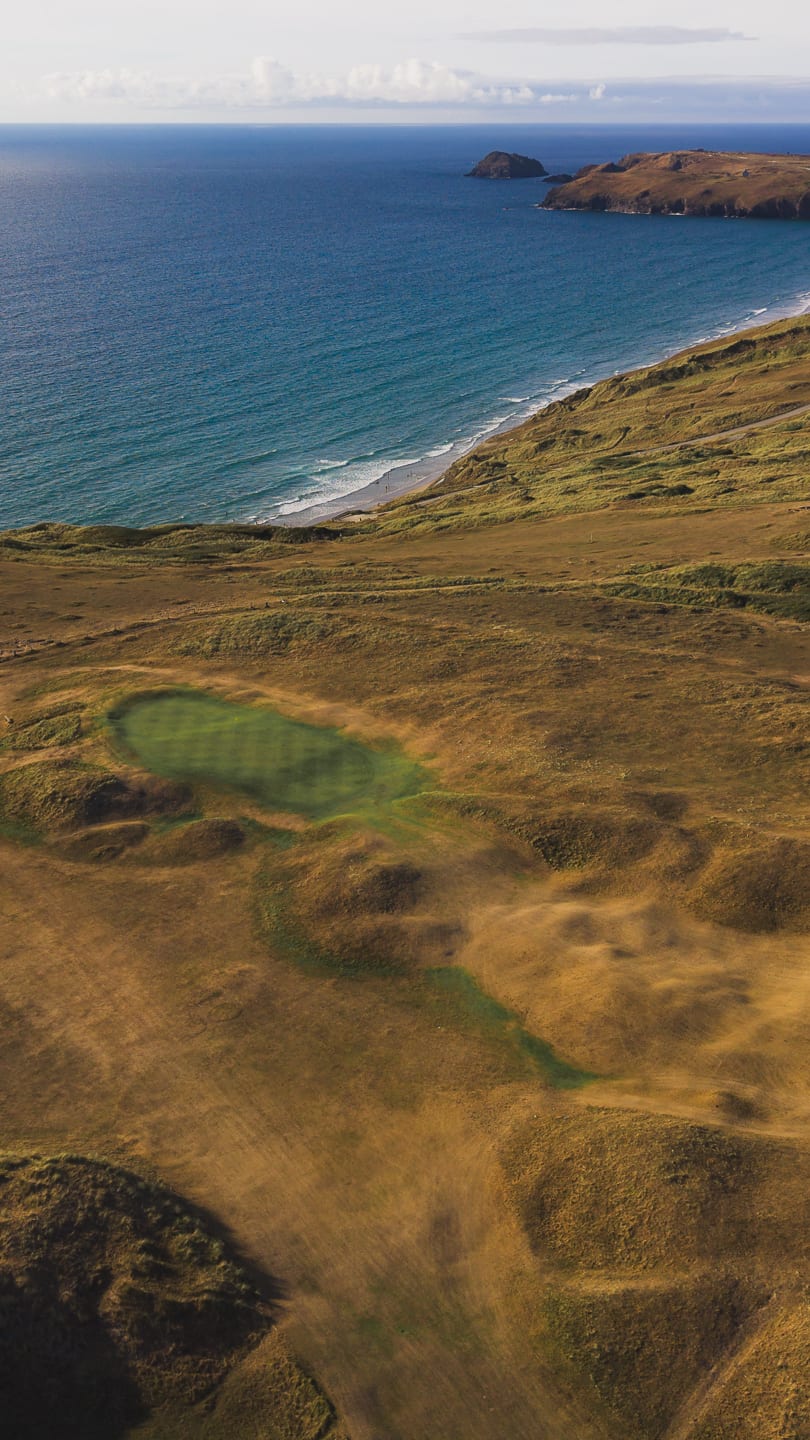 A green in the dunes above the beach at Newquay, seen from the air with the headland beyond