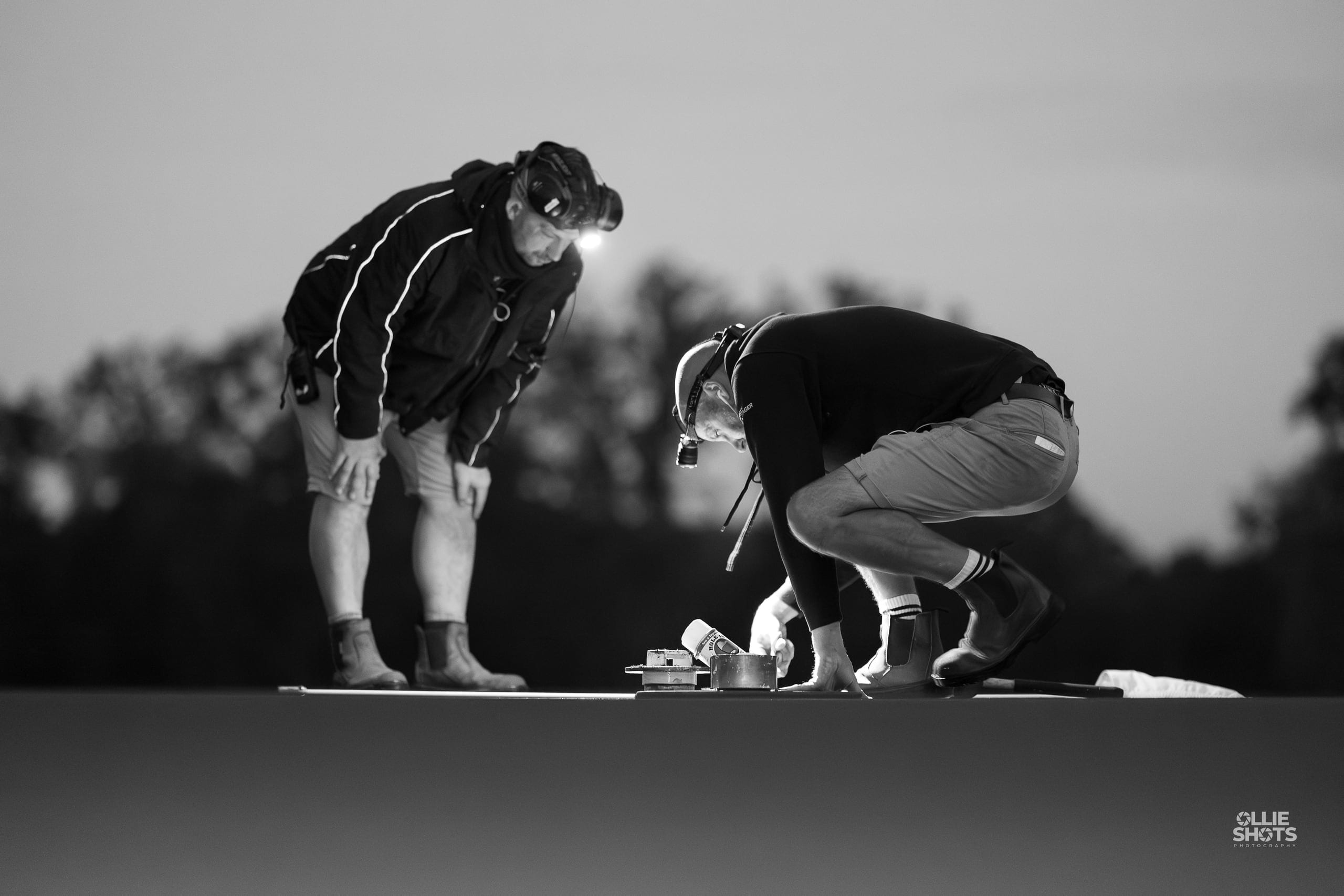 A greenkeeper crouched with a dog on the green, black and white