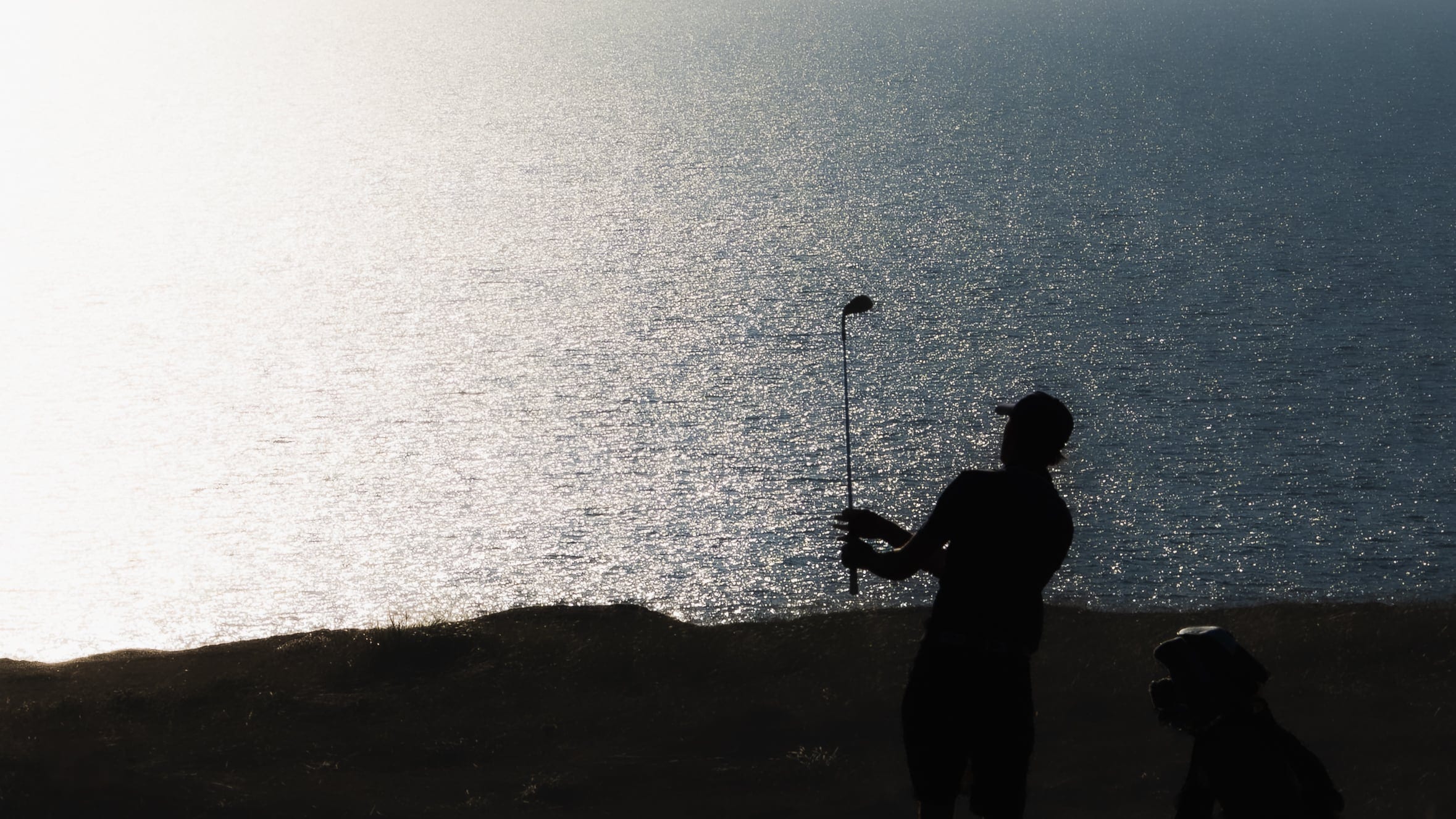 A golfer and a dog silhouetted against the sea, black and white