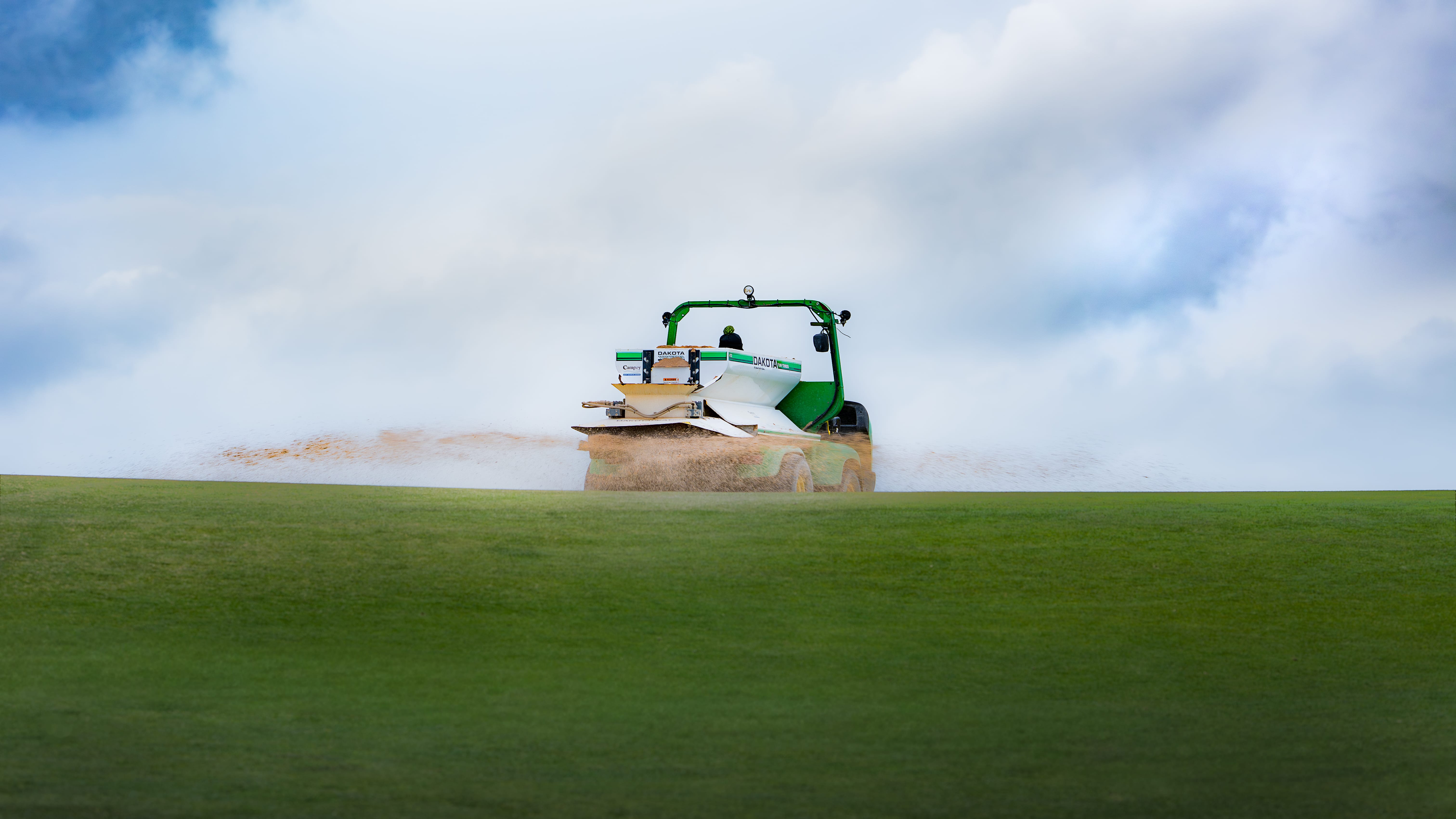 A topdresser spreading sand across a green, the maintenance work members rarely see