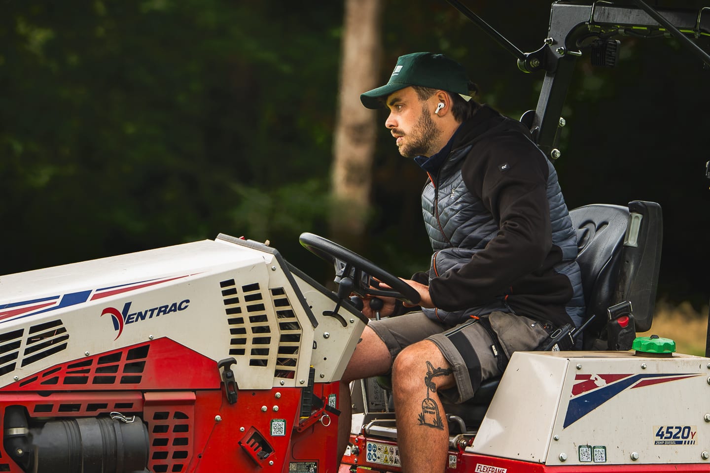 A greenkeeper at the controls of a compact utility tractor