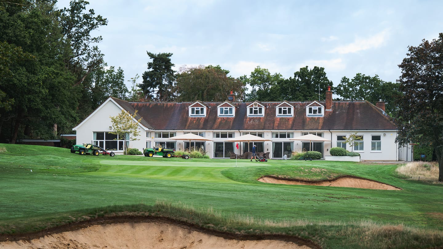The clubhouse behind the 18th green, greenkeepers tending the green and bunkers