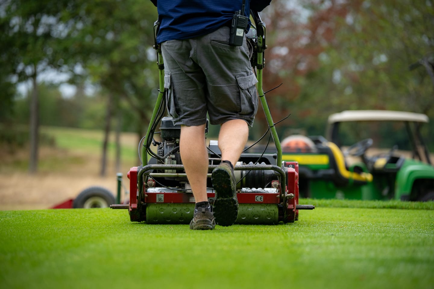 A greenkeeper walking a mower away towards a parked buggy