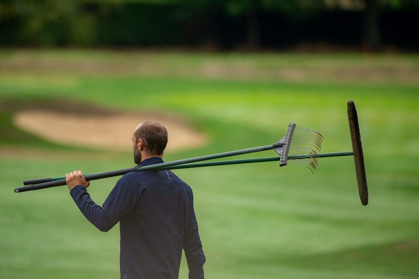 A greenkeeper carrying a bunker rake over his shoulder